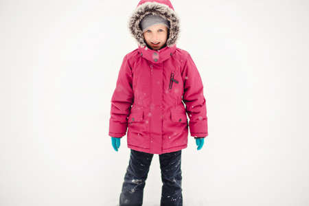 Portrait of cute funny Caucasian smiling girl child in warm clothes red pink jacket playing with...