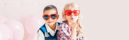 Valentine day holiday celebration. Web header banner for website. Two happy Caucasian cute funny children wearing heart shape sunglasses. Boy and girl hugging. Love, friendship and fun.の写真素材