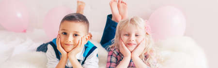 Happy Caucasian funny children lying on bed. Best friends forever. Valentine Day holiday concept. Web banner header for website. Boy and girl having fun making faces. Love and friendship.の写真素材