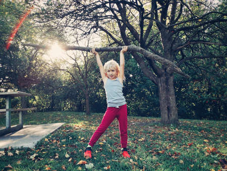 Sporty healthy strong young girl lifting wooden stick branch log in park. Cute kid playing outdoor on summer autumn fall day. Powerful female child girl lifting weights outside.の写真素材