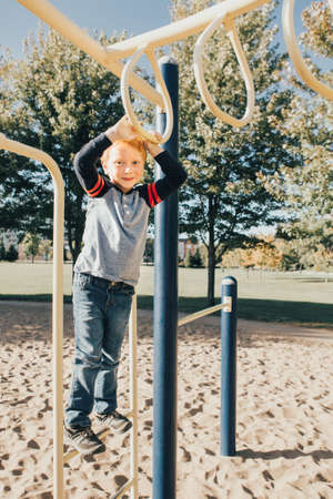 Young Caucasian boy hanging on monkey bars in park on playground. Summer outdoor activity for kids....