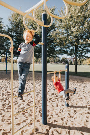 Young Caucasian boys friends hanging on monkey bars and pull-up bars in park on playground. Summer outdoor activity for kids. Active children doing exercises sport. Healthy happy childhood. の写真素材