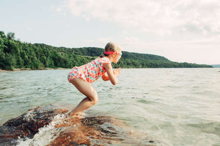 Cute funny Caucasian girl diving in lake with underwater goggles. Child swimming in water on beach. Authentic real lifestyle happy childhood. Summer fun outdoor aquatic seasonal sport activity.の写真素材