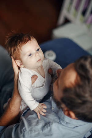 Proud Caucasian father talking to newborn baby girl. Parent holding rocking child daughter in hands....