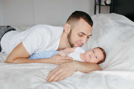 Caucasian father lying with newborn baby in bedroom. Man parent hugging kissing embracing child...