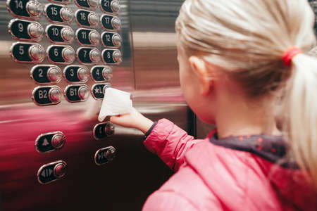 Caucasian girl pushing elevator button with disinfecting wet wipe. Precaution against virus spread....
