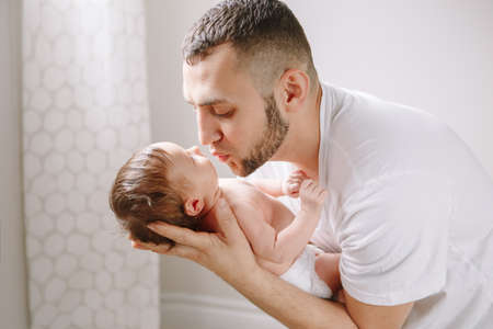 Happy young Caucasian father kissing newborn baby. Dad man parent holding rocking child daughter son...