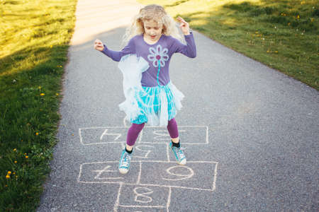 Cute adorable little young child girl playing hopscotch outdoor. Funny activity game for kids on playground outside. Summer backyard street sport for children. Happy childhood lifestyle.の写真素材