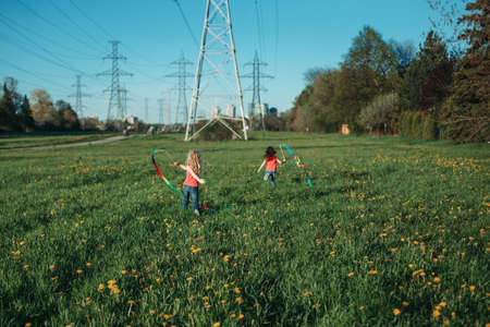 Happy children girls playing with ribbons in park. Cute adorable kids running on meadow playing together. Outdoor summer backyard activity for kids. Happy childhood candid authentic lifestyle. の写真素材