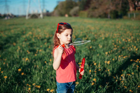 Preschool Caucasian girl blowing soap bubbles in park on summer day. Child having fun outdoor. Authentic happy childhood magic moment. Lifestyle seasonal activity for children.の写真素材