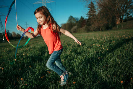 Happy child girl playing with ribbons in park. Cute adorable kid running on meadow playing together. Outdoor summer backyard activity for kids. Innocent childhood candid authentic lifestyle. の写真素材