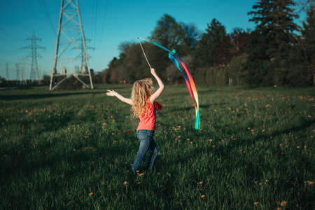 Happy child girl playing with ribbons in park. Cute adorable kid running on meadow playing together. Outdoor summer backyard activity for kids. Innocent childhood candid authentic lifestyle.の写真素材