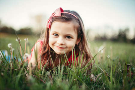 Cute adorable Caucasian girl among dandelions flowers. Child lying in grass on meadow. Outdoor fun summer seasonal children activity. Kid having fun outside. Happy childhood lifestyle.の写真素材