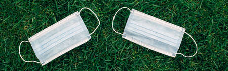 Two fresh new sanitary masks lying on grass. Disposable recyclable face mask flat lay. Coronavirus, medicine and seasonal allergy concept. View from top. Banner header for website.の写真素材