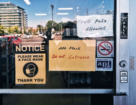 Toronto, Ontario, Canada - June 11, 2020: Warning notice on store shop door window saying to wear protection face mask when entering. Precaution against coronavirus covid-19 spread. New normal rules.のeditorial素材