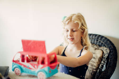 Cute little girl playing toy car bus with dolls. Active little child kid playing alone on a quarantine at home. Happy authentic real childhood lifestyle.の写真素材