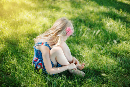 Sad young girl sitting on ground outdoor on summer sunny day. Pensive little child dreaming thinking. Insecure lonely kid trying to cope with stress problems. Authentic childhood lifestyle.の写真素材