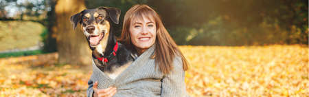 Happy young Caucasian woman hugging dog. Owner walking with pet on autumn fall day. Best friends...