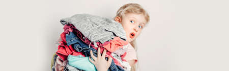 Mommy little helper. Funny cute girl child arranging organazing clothing. Kid holding messy stack pile of clothes things. Home chores housework. Web banner header for website.の写真素材