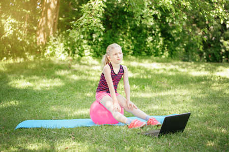 Caucasian girl child doing sport workout outdoor online. Video yoga stretching on Internet. Kid...