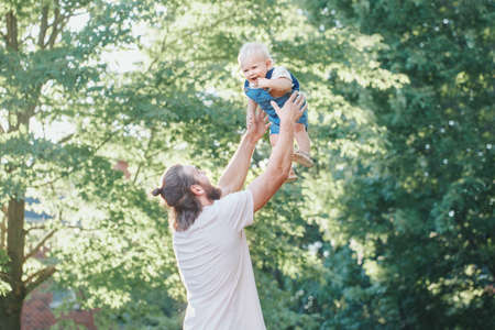 Proud father playing with toddler baby boy outdoor. Parent holding tossing up lifting child son up in air. Authentic lifestyle tender moment. Single dad family life concept. Happy fatherhood.の写真素材