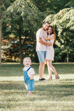 Happy smiling mother and father with baby boy in park outdoor. Family Caucasian mom and dad with son walking hugging in park on summer day. Happy family authentic lifestyle concept.の写真素材