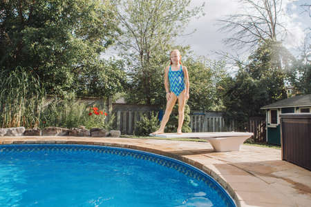 Cute red-haired girl diving in pool from springboard. Child kid enjoying having fun in swimming pool...