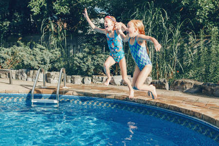 Girls sisters diving in water on home backyard pool. Children siblings friends enjoying and having fun in swimming pool together. Summer outdoor water activity for kids.の写真素材