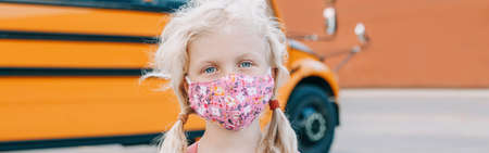 Caucasian girl student wearing face mask by yellow school bus. Kid with personal protective...