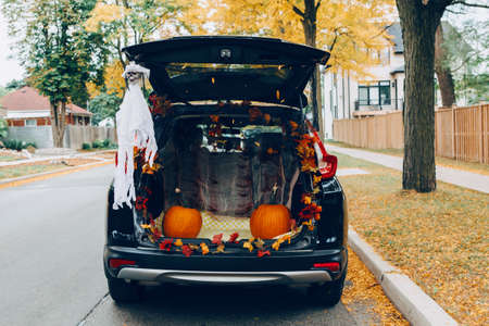 Trick or trunk. Black car trunk decorated for Halloween. Autumn fall decor with red pumpkins and yellow leaves for traditional October holiday outdoor. Social distance during coronavirus covid-19.の写真素材