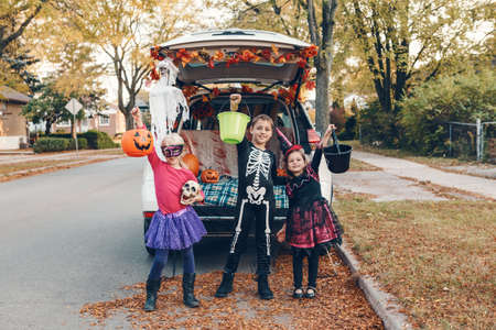 Trick or trunk. Siblings brother and sisters celebrating Halloween in trunk of car. Children kids boy and girls preparing for October holiday outdoor. Social distance and safe alternative celebration.の写真素材