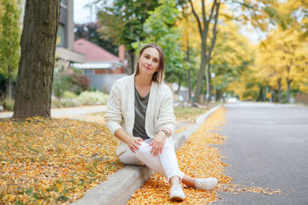 Beautiful middle age Caucasian woman with short hair sitting in autumn fall street outdoor. Young...
