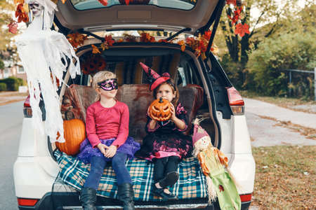 Trick or trunk. Children siblings sisters celebrating Halloween in trunk of car. Friends kids girls preparing for October holiday outdoor. Social distance and safe alternative celebration.の写真素材