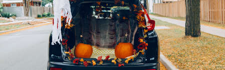 Trick or trunk. Black car trunk decorated for Halloween. Autumn fall decor with red pumpkins and yellow leaves for traditional October holiday outdoor. Web banner header.の写真素材