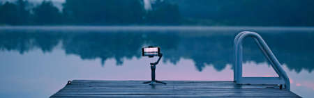 New technology. Smartphone standing on gimbal tripod outdoor for stabilisation video. Modern tool camera equipment for bloggers and vloggers. Web banner header.の写真素材