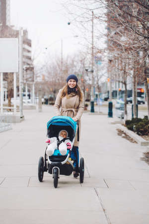 Happy young Caucasian mother walking with baby daughter outdoor in Toronto. Family two people strolling together outside on city street. Urban life with kids children.の写真素材