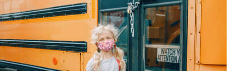 Sad girl student with face mask near locked yellow bus. Closed school during pandemic and quarantine shutdown. New normal education in coronavirus. Web banner header.の写真素材
