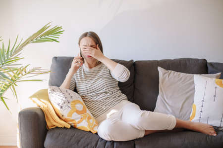 Sad upset middle age woman talking on mobile phone. Bad news and negative reaction emotion. Young crying woman talking over smartphone and covering her eyes with hand.の写真素材