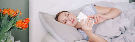 Middle age woman lying in bed with smartphone surfing Internet. Young woman talking with friends in...