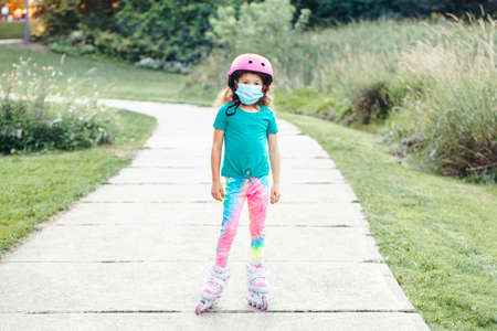 New normal. Girl in face protective mask riding in roller skates on road in park on summer day....