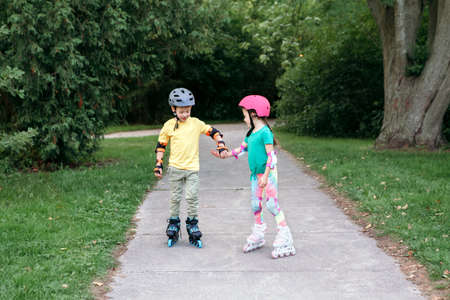 Happy Caucasian friends boy and girl riding on roller skates in park on summer day. Seasonal outdoor children activity sport. Healthy childhood lifestyle. Kids individual summer sport.の写真素材