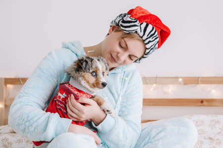 Young woman in Santa hat hugging cute miniature Australian shepherd puppy dog pet. Pet owner celebrating Christmas holiday alone. Holiday celebration together with furry little friend.の写真素材