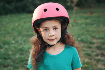 Closeup portrait of adorable pretty cute Caucasian girl in pink helmet in park on summer day....