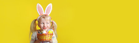 Caucasian blonde girl with pink Easter bunny ears holding eggs. Person in studio on yellow...