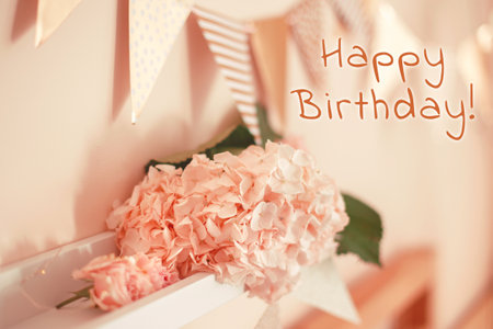 Happy Birthday card with greeting text. Room decoration in pink beige neutral colors for birthday celebration. Macro closeup of light pink hydrangea flowers and triangle flags on shelf for party.の写真素材