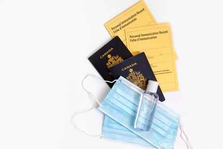 Two Canadian passports with yellow immunity vaccination records, face sanitary blue masks and sanitizer. Safety measures against coronavirus covid-19 spread. Mandatory vaccine for traveling.の写真素材