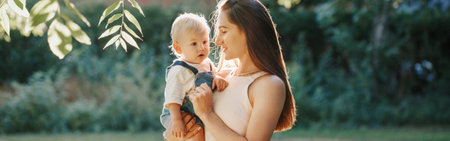 Mothers Day. Young smiling Caucasian mother and boy toddler son hugging in park. Mom holding carrying child baby on hands outdoor. Happy authentic family childhood lifestyle. Web banner header.の写真素材