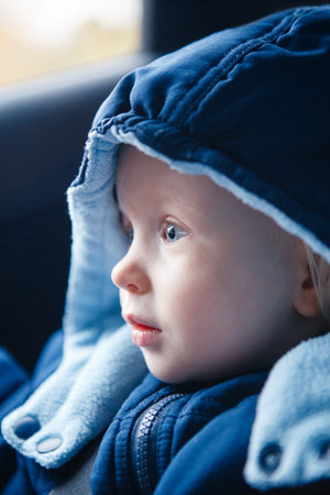 Cute Caucasian baby infant sitting in car seat. Adorable kid in outwear clothes in automobile vehicle carsit fastened with seatbelt. Care, safety and protection of children on roads.の写真素材
