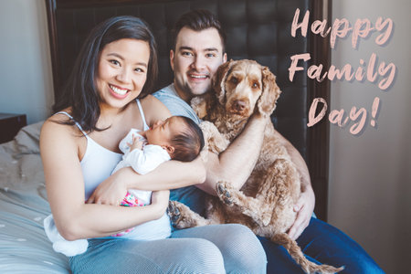 Happy Family Day. Holiday card with greeting text. Smiling Chinese Asian mother and Caucasian father with newborn baby and pet dog. Home lifestyle authentic natural moment.の写真素材