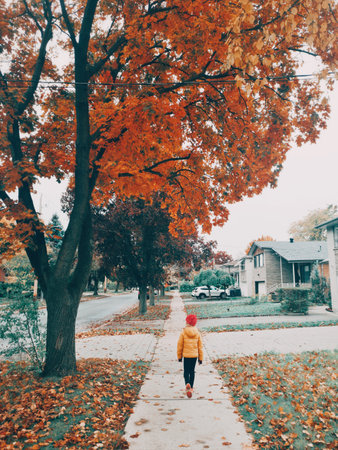 Cute girl child in yellow jacket and pink hat walking down the street in suburbs outdoor. Kid...